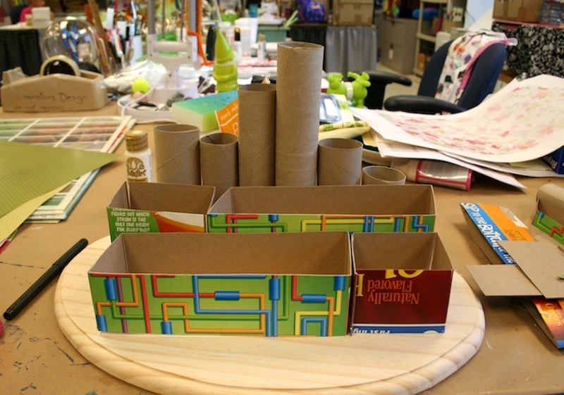 Cereal box pieces and toilet paper rolls and paper towel rolls sitting on the top of a wood plaque