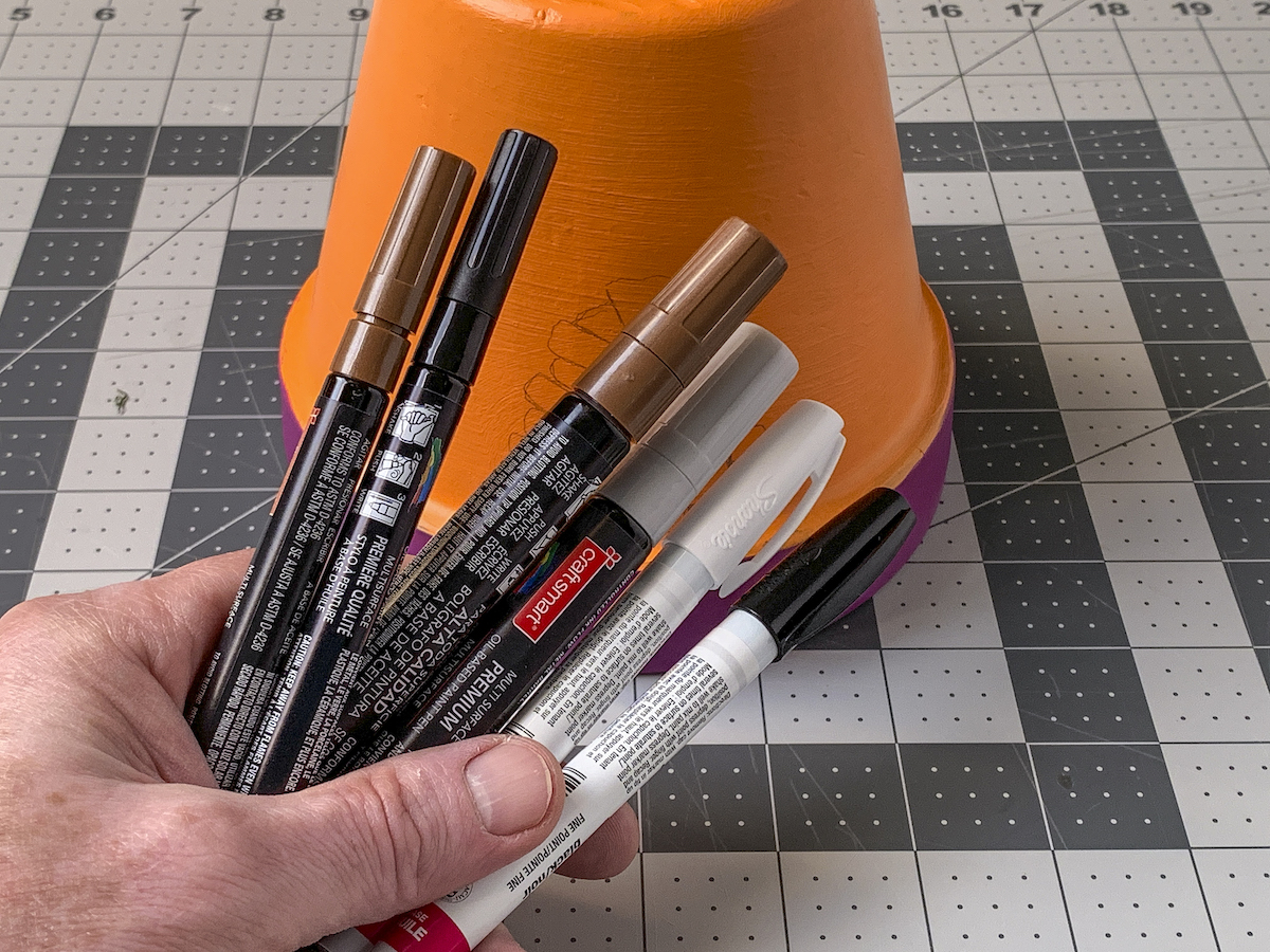 Hand holding paint pens in brown, black, and white