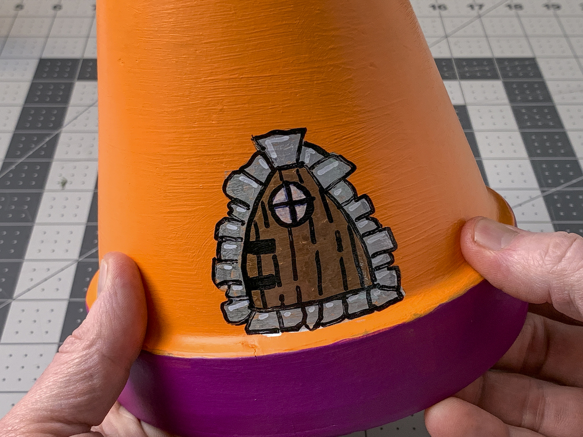 Hands holding a clay pot painted with a fairy door