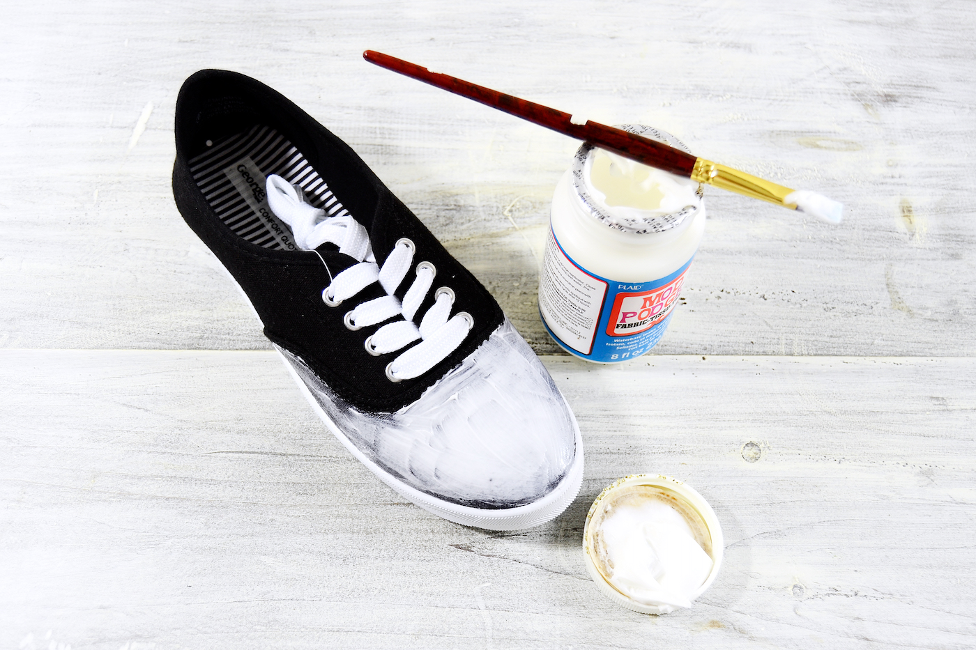 Mod Podge being applied to the front of a black shoe