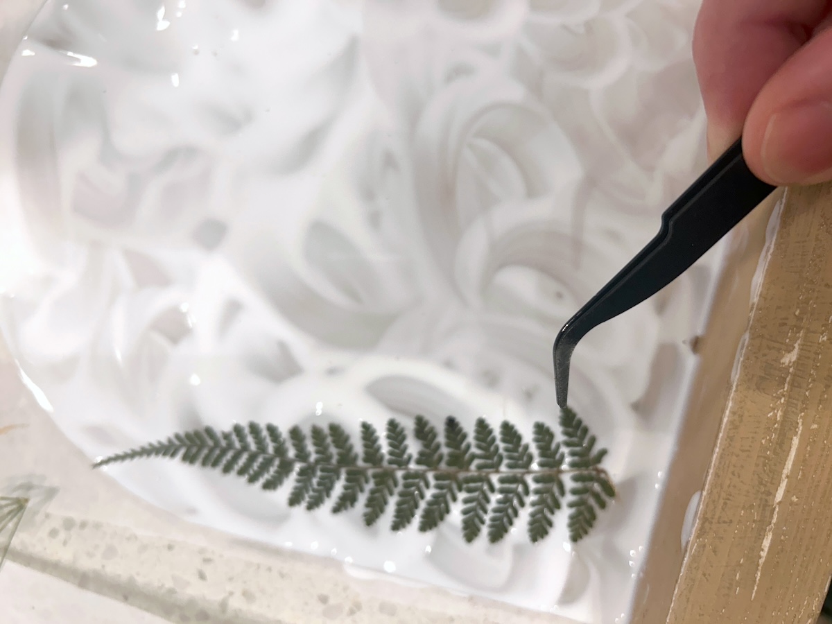 Placing a small fern down into Mod Podge with tweezers